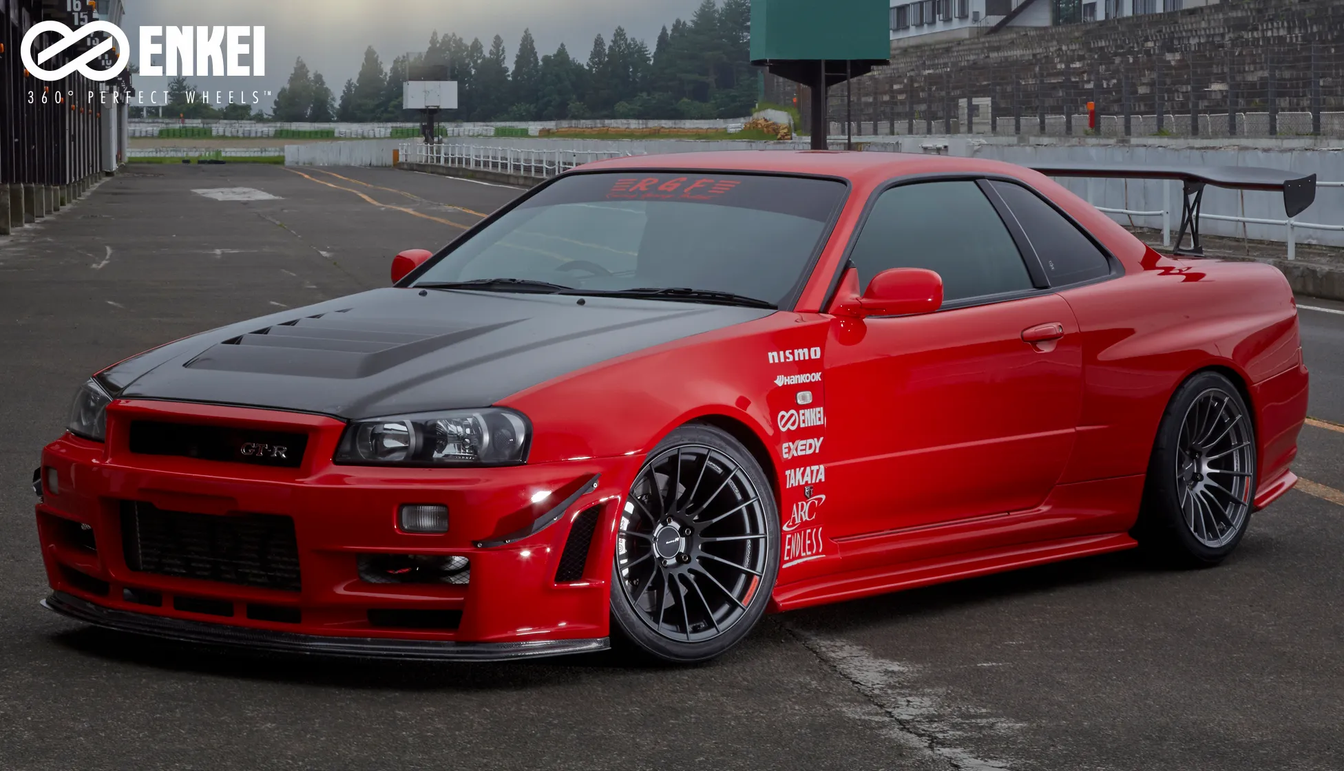 赤い日産スカイラインGT-R R34にダークカラーのホイールを装着したサーキットでの写真