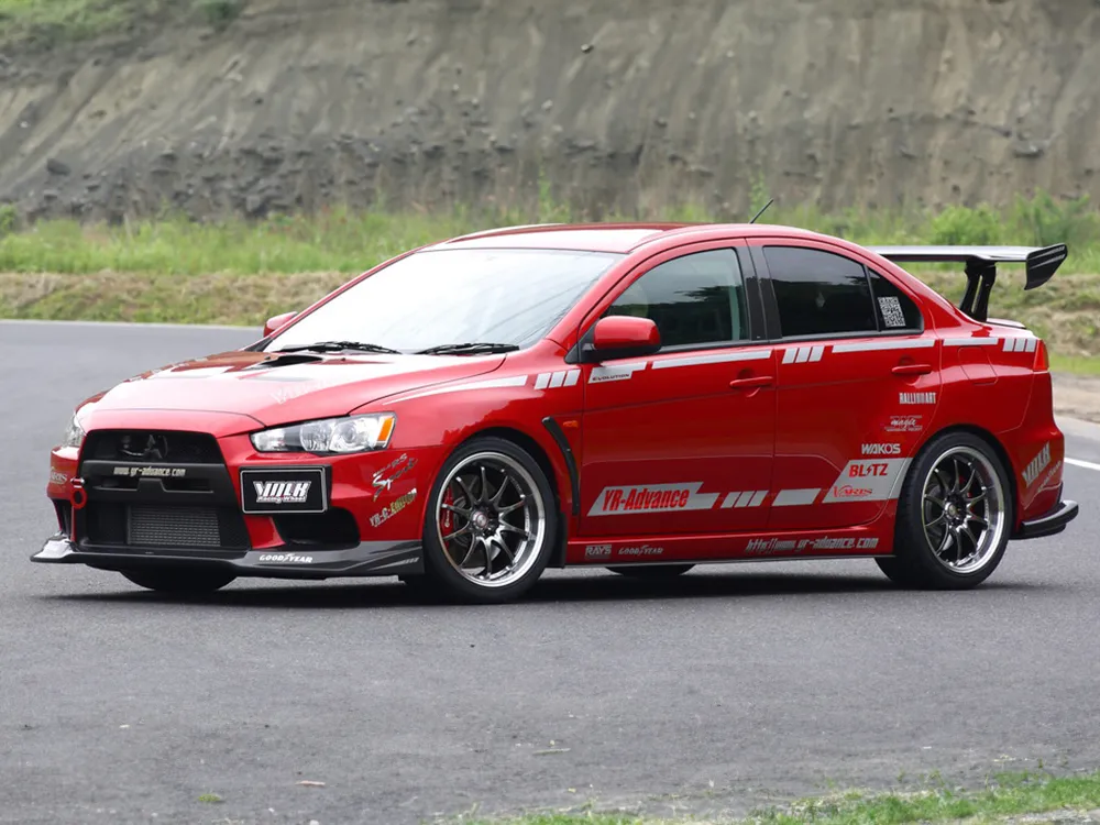 サーキットを走る赤い三菱ランサーエボリューションX。濃色ホイールと大型リアウイングが見える右前方からの写真