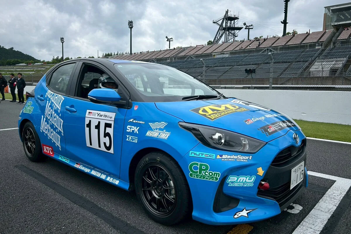 サーキットに停車するゼッケン115の青いトヨタ・ヤリスカップ車両と黒いスポーツホイール